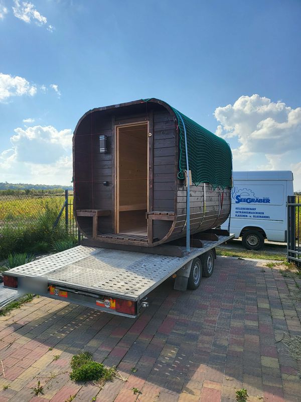 Sauna z otwartym przedsionkiem zabezpieczona siatką na przyczepie, gotowa do transportu