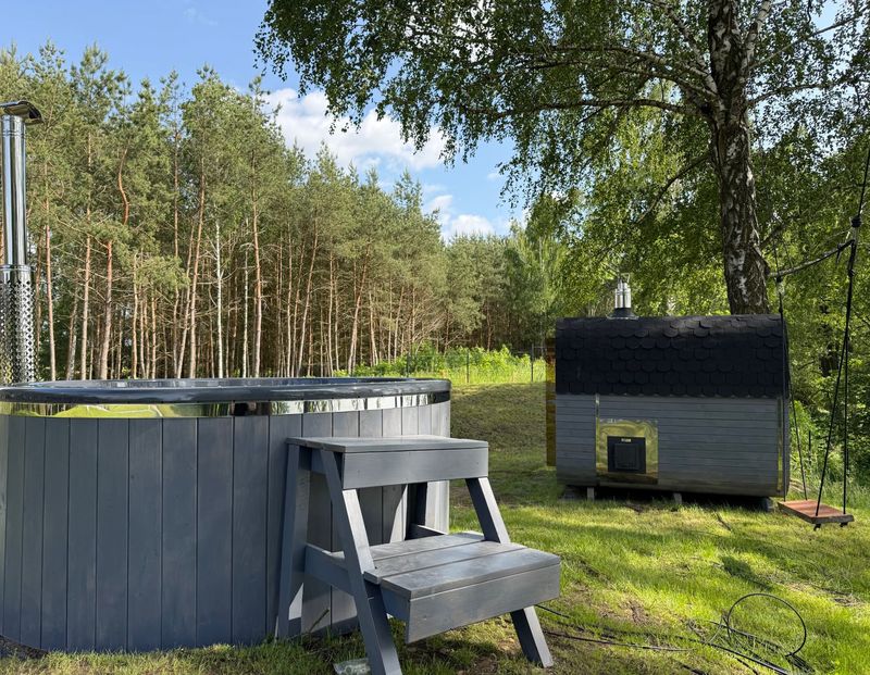 Grafitowa balia okrągła ze schodkami w lesie sosnowym, w tle grafitowa sauna
